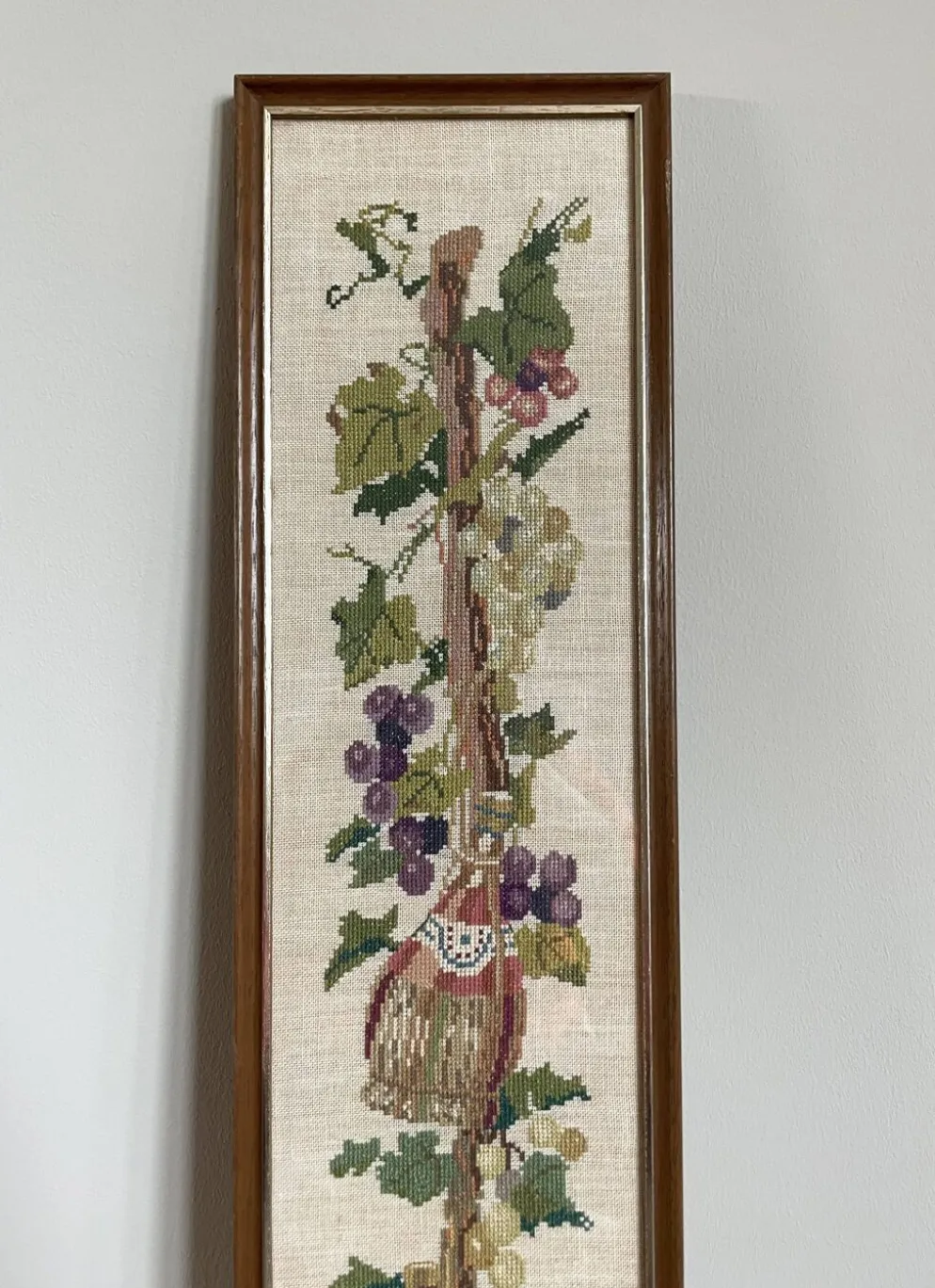 Broderie néerlandaise encadrée représentant une vigne avec des raisins, des bouteilles de vin et des paniers.