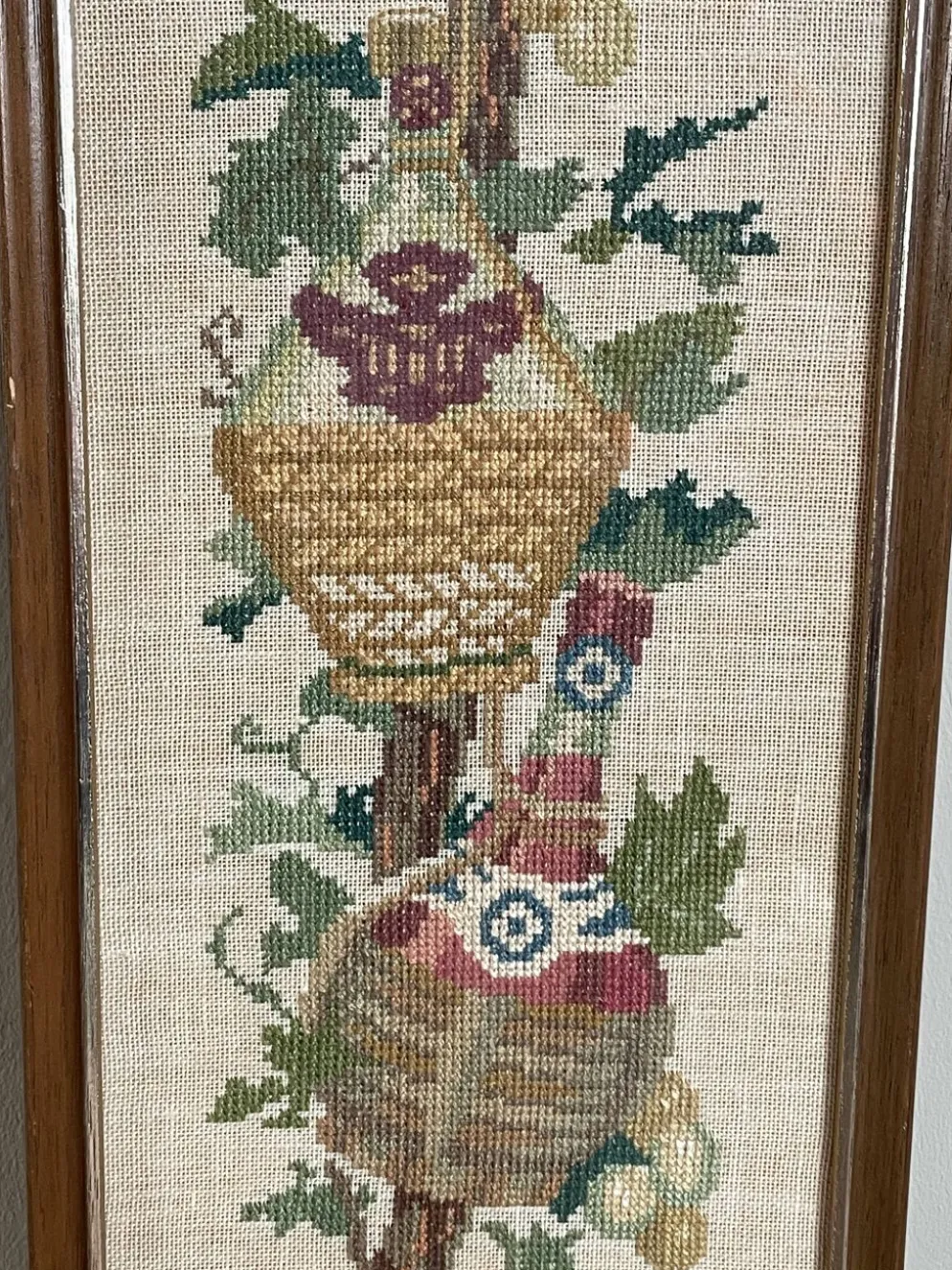 Broderie néerlandaise encadrée représentant une vigne avec des raisins, des bouteilles de vin et des paniers.