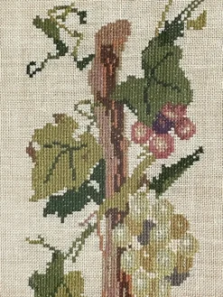Broderie néerlandaise encadrée représentant une vigne avec des raisins, des bouteilles de vin et des paniers.