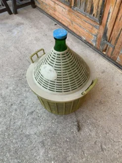 Grande dame‑jeanne en verre vert dans panier plastique kaki style mid‑century